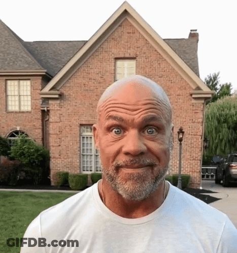 A Bald Man With A Beard Stands In Front Of A Large Brick House GIF
