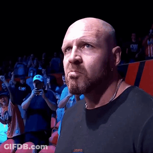 A Bald Man With A Beard Wearing A Black Shirt Stands In Front Of A Crowd With The Word Jafo On The Bottom Left GIF
