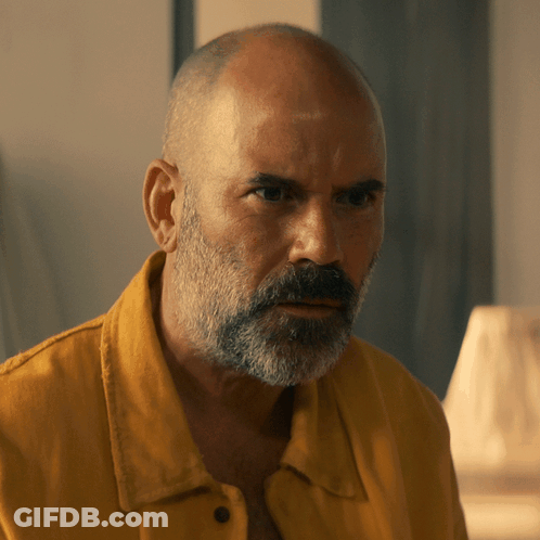 A Bald Man With A Beard Wearing A Yellow Shirt Looks At The Camera GIF