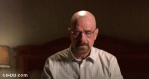 A Bald Man With A Beard Wearing Glasses Is Sitting In Front Of A Bed GIF