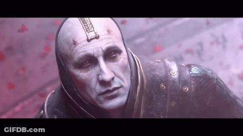 A Bald Man With A Hood On His Head Is Standing In Front Of A Red Wall . GIF