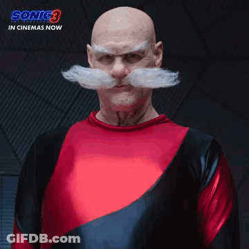 A Bald Man With A Mustache And A Red Shirt Is Standing In Front Of A Sign That Says The Robotniks GIF