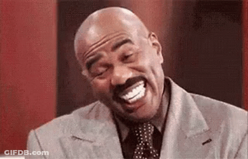 A Bald Man With A Mustache Is Laughing With His Mouth Open While Wearing A Suit And Tie . GIF