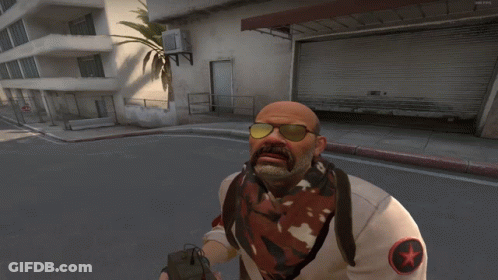 A Bald Man With A Mustache Wearing Sunglasses And A White Shirt With A Red Star On It GIF