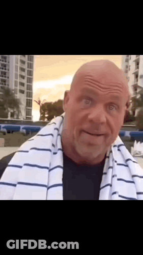 A Bald Man With A Striped Towel Around His Neck Looks At The Camera . GIF