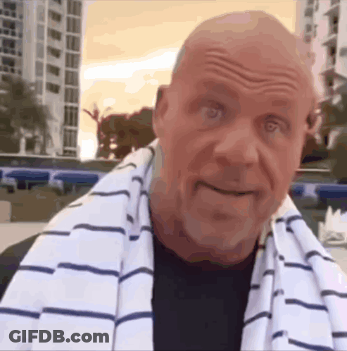 A Bald Man With A Striped Towel Around His Neck Looks At The Camera GIF