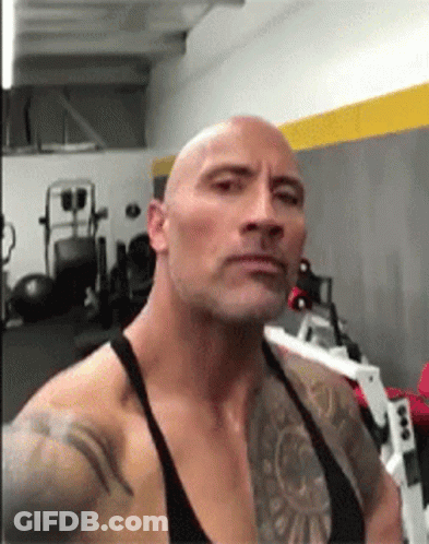 A Bald Man With A Tattoo On His Arm Is Standing In A Gym . GIF