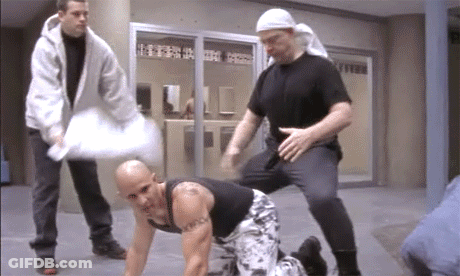 A Bald Man With A Tattoo On His Chest Is Kneeling Down GIF