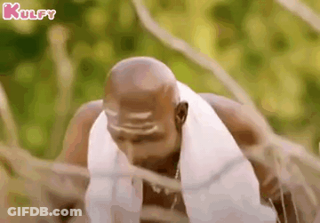 A Bald Man With A Towel Around His Neck Is Standing In A Forest . GIF