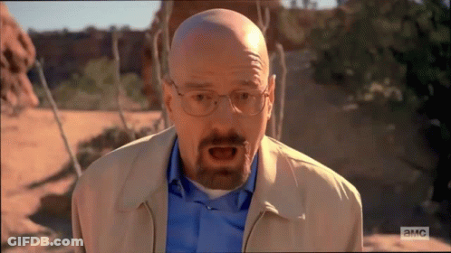 A Bald Man With Glasses And A Beard Is Standing In A Desert . GIF