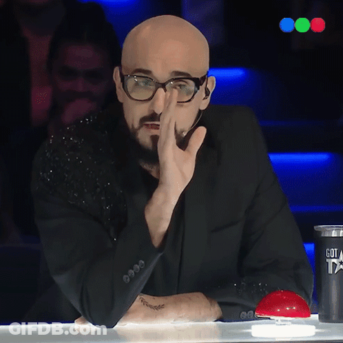 A Bald Man With Glasses And A Tattoo On His Arm Is Sitting At A Table GIF