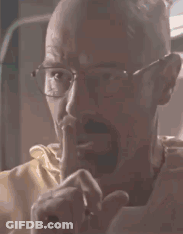 A Bald Man With Glasses Is Holding His Finger To His Mouth . GIF