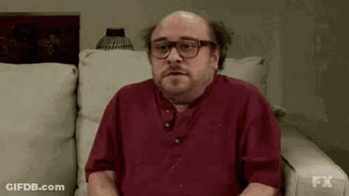 A Bald Man With Glasses Is Sitting On A Couch With His Mouth Open . GIF