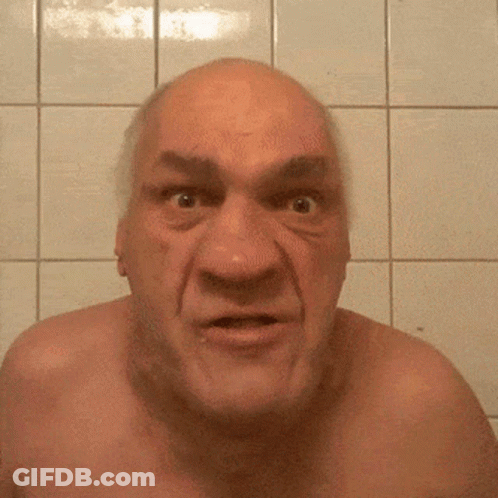 A Bald Man Without A Shirt Is Making A Funny Face In Front Of A Tiled Wall GIF