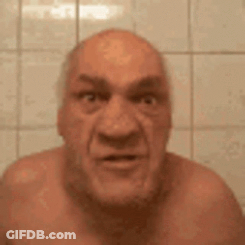A Bald Man Without A Shirt Is Making A Funny Face While Standing In Front Of A Tiled Wall . GIF