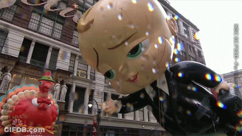 A Balloon Of A Baby In A Suit Is Floating In Front Of A Building That Says Macy 'S GIF