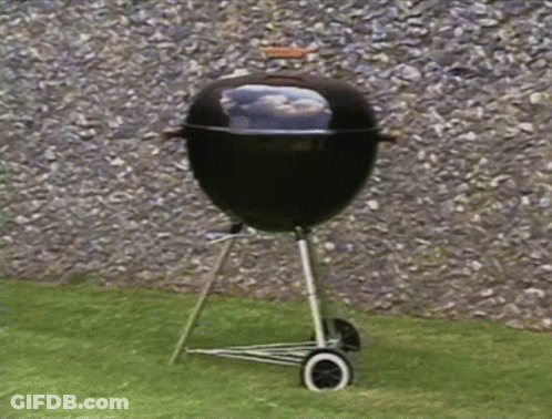 A Barbecue Grill Is Sitting On A Lawn In Front Of A Rock Wall GIF