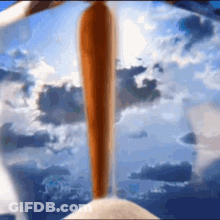 A Baseball Bat Is Flying Through The Air In Front Of A Blue Sky With Clouds . GIF