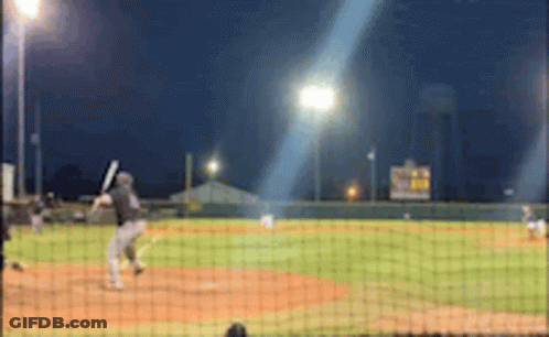 A Baseball Game Is Being Played At Night And A Batter Is Swinging His Bat GIF