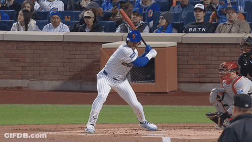A Baseball Player Getting Ready To Swing At A Pitch While A Fan Wearing A Brtn Shirt Watches GIF