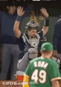 A Baseball Player In A Green Jersey Is Giving A High Five To Another Player . GIF