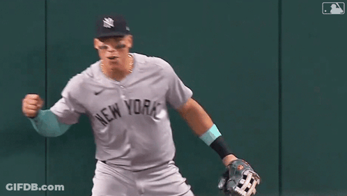 A Baseball Player In A New York Yankees Uniform Is Running On The Field With His Fist In The Air . GIF