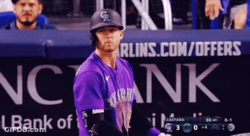 A Baseball Player In A Purple Uniform Stands In Front Of A Bank Of America Sign GIF