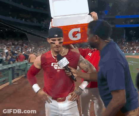 A Baseball Player Is Being Interviewed By A Reporter While Holding A Gatorade Cooler On His Head GIF