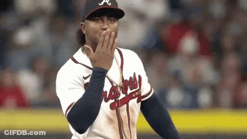 A Baseball Player Is Covering His Mouth With His Hand While Standing On A Field . GIF