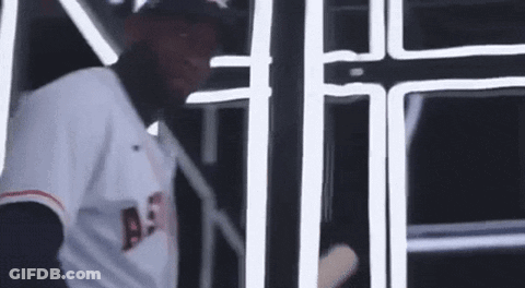 A Baseball Player Is Holding A Bat In A Dark Room . GIF
