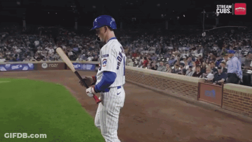 A Baseball Player Is Holding A Bat In Front Of A Stream Cubs Sign GIF