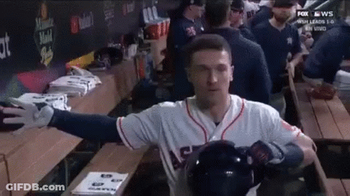 A Baseball Player Is Standing In A Dugout With His Arms Outstretched And Holding A Helmet . GIF