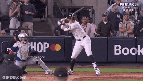 A Baseball Player Is Swinging At A Pitch In Front Of A Wall That Says Hop And Book GIF