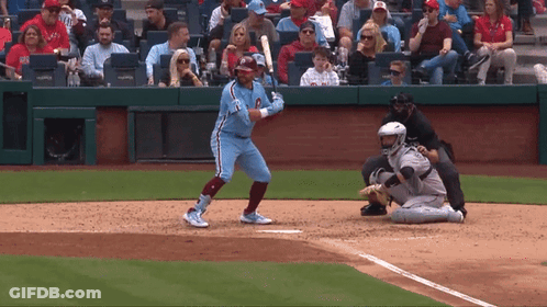 A Baseball Player Is Swinging His Bat At A Ball While A Catcher Watches GIF