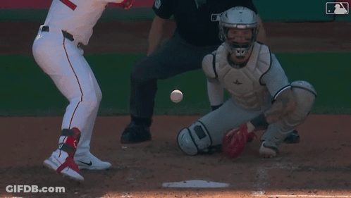 A Baseball Player Is Swinging His Bat At A Ball While The Catcher Watches GIF