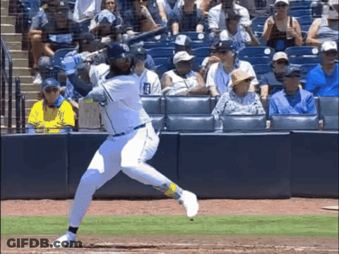 A Baseball Player Is Swinging His Bat At A Ball With A Crowd Watching GIF