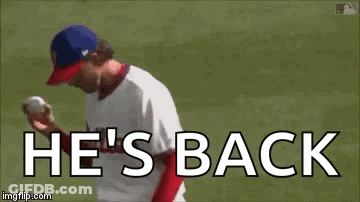 A Baseball Player Is Throwing A Ball On A Field With The Words `` He 'S Back '' . GIF