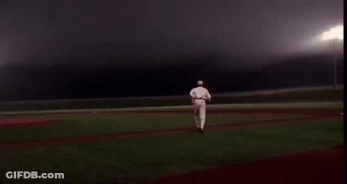 A Baseball Player Is Walking Across A Baseball Field At Night . GIF