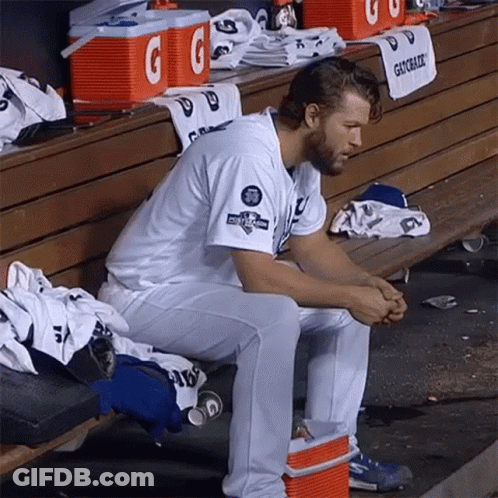 A Baseball Player Sits On A Bench In The Dugout With Gatorade Coolers In The Background GIF