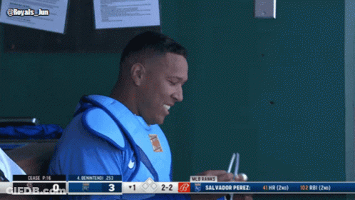 A Baseball Player Sitting In The Dugout With A Scoreboard Behind Him That Says Mlb Ranks GIF