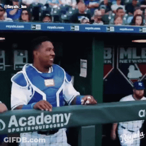 A Baseball Player Stands Behind A Fence That Says Academy Sports & Outdoors GIF