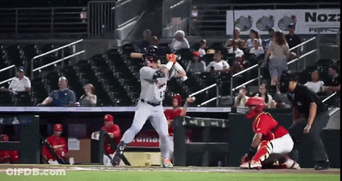 A Baseball Player Swings At A Pitch In Front Of An Advertisement For Nozz GIF