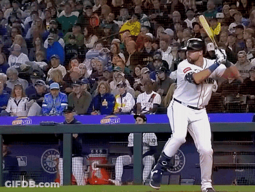 A Baseball Player Swings His Bat At A Ball In Front Of A Crowd With A Banner That Says Coca Cola GIF