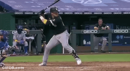 A Baseball Player Swings His Bat At A Ball In Front Of A Geico Sign GIF