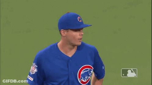 A Baseball Player Wearing A Blue Cubs Uniform Is Standing On A Green Field . GIF