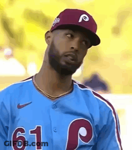 A Baseball Player Wearing A Blue Jersey And A Red Hat Is Looking At The Camera . GIF