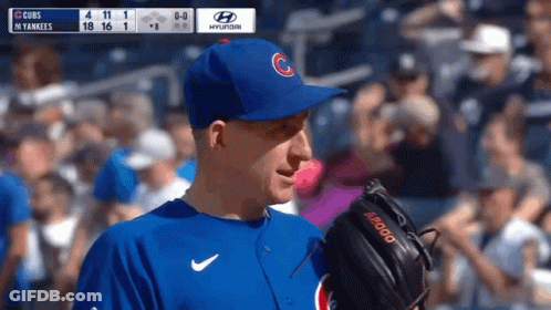 A Baseball Player Wearing A Cubs Hat Stands In Front Of A Scoreboard GIF