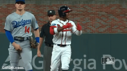 A Baseball Player Wearing A Dodgers Jersey Stands Next To An Atlanta Braves Player GIF