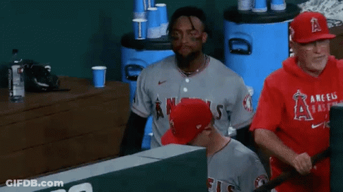 A Baseball Player Wearing A Gray Angels Jersey Is Sitting In The Dugout . GIF