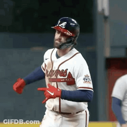 A Baseball Player Wearing A Helmet And Gloves Is Pointing At Something While Running On The Field . GIF